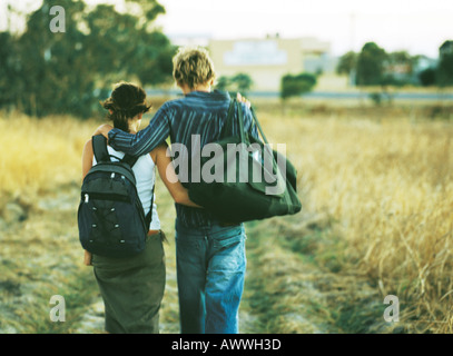 Paare, die Arme umeinander durch Feld, Rückansicht Stockfoto