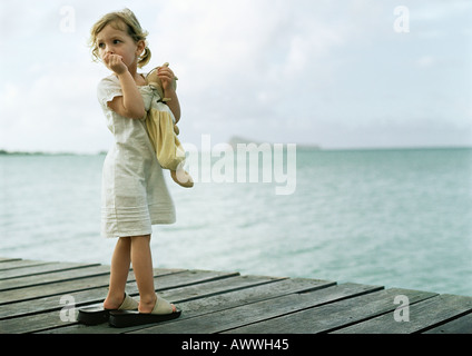 Kleines Mädchen stand auf Dock, Daumenlutschen und sah über die Schulter Stockfoto