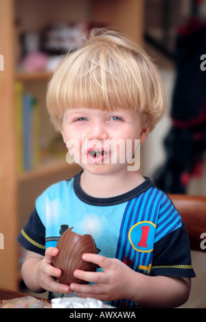 Blonde behaarte junge Essen und genießen Sie Schokoladen Osterei und lächelnd Stockfoto