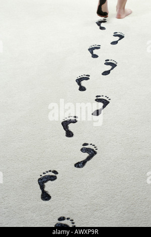 Junge Frau verlassen schwarze Fußspuren auf Teppich Stockfoto
