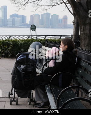 Eine Mutter und Ihr Baby sitzen neben dem Hudson River in Battery Park City an einem kühlen Tag im März. Stockfoto