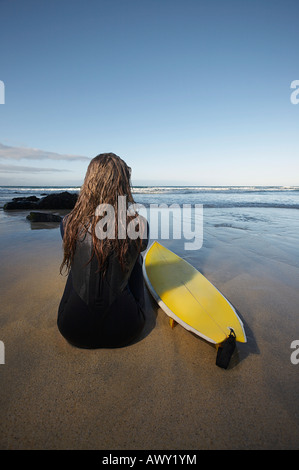 Frau sitzt mit Surfbrett am Strand wieder anzeigen Stockfoto