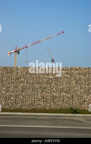 Baukräne hinter einer Wand aus weißen Steinen Stockfoto