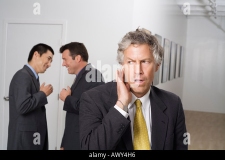 Geschäftsmann, hören von Kollegen tratschen im Flur Stockfoto