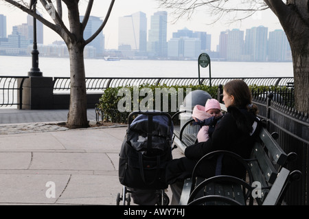 Eine Mutter und Ihr Baby sitzen neben dem Hudson River in Battery Park City an einem kühlen Tag im März. Stockfoto