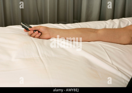 Mann auf Bett, mit einem Handy in der Hand, Fokus auf arm Stockfoto