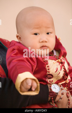 Eine Glatze chinesischen Jungen in eine rote Seide Jacke, statt sich von seiner Mutter geleitet. Stockfoto