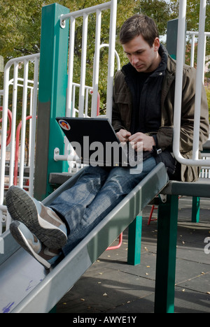 Junger Mann, der auf seinem Laptop in Brooklyn NewYork Spielplatz arbeitet Stockfoto