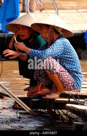 Asien Fernost Vietnam, Hoi an Markt, zwei alte Damen in non nai tho, konische Hüte, tief in der Unterhaltung auf den Tagen Handel mit Wasser rauchen Stockfoto