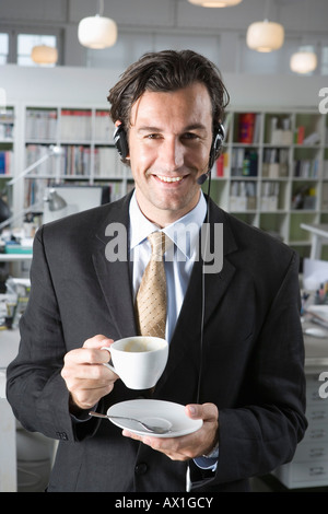 Ein Mann trägt einen Telefon-Kopfhörer und hält eine Tasse Kaffee Stockfoto