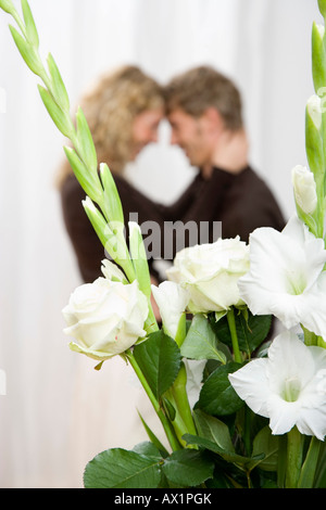 Ein paar umarmt hinter einem Bouquet aus weißen Schwert Lilien und Rosen Stockfoto