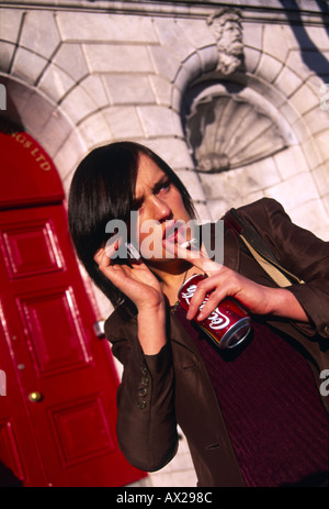 Betonte junge Frau Rauchen und trinken Coca Cola während des Gesprächs auf ihrem Mobiltelefon Stockfoto