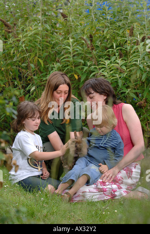ZWEI KINDER BEI IHRER MUTTER ZU ERFÜLLEN EIN KANINCHEN IM STREICHELZOO IM LONGLEAT SAFARI PARK IN DER NÄHE VON WARMINSTER WILTSHIRE Stockfoto
