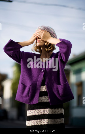 Frau bedeckte ihr Gesicht mit gekauften Händen trägt einen lila Mantel über einen Bodensatz in schwarzen und weißen Streifen Stockfoto