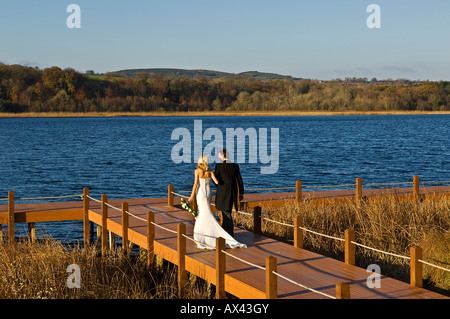 Großbritannien, Nordirland, Fermanagh, Enniskillen. Braut und Bräutigam gehen Arm in Arm auf dem Ponton während ihrer Hochzeit am Lough Erne Golf Resort Hotel (MR). Stockfoto