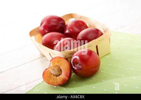 roten Pflaumen im kleinen Korb, ganz und halb grün vor, Tuch auf dem Tisch Stockfoto