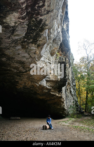 Mädchen sitzen alleine auf einem Baumstamm unter Felsen vor Höhle Stockfoto