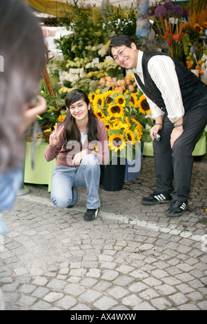 Person, die ein Bild von einem asiatischen Mann und einer asiatischen Frau vor einer Blume-Stand (Teil), Fokus auf Hintergrund Stockfoto