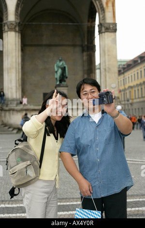 Asiatischer Mann filmt sich und seine Frau mit einer Kamera, während sie vor einem Denkmal, selektiven Fokus stehen Stockfoto