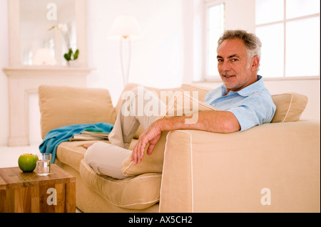 Reifer Mann sitzt auf dem Sofa im Wohnzimmer, Porträt Stockfoto