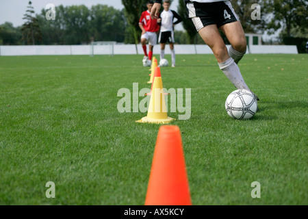 Fußball-Spieler läuft mit Fußball Slalom um Pylonen Stockfoto