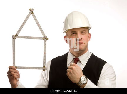 Mann in Anzug hält Maßstab zu einem Haus geformt Stockfoto