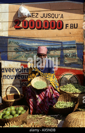 Gitega, Burundi. Frau im Markt verkaufen Erbsen und Obst vor einer bemalten Wand mit Bildern; Französische Wörter. Stockfoto