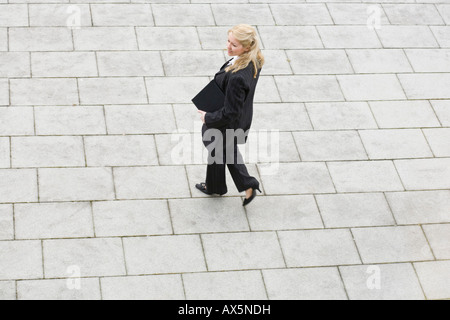 Geschäftsfrau mit Aktentasche unter dem Arm, zu Fuß über ein leeres Quadrat Stockfoto
