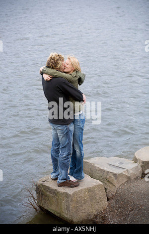 Paar steht auf einem Felsen am Rand des Wassers, umarmen einander Stockfoto