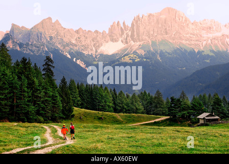 Zwei Frauen Wandern auf einem Weg durch eine Wiese am Abend Rosengarten Alpen im Hintergrund, Bolzano-Bozen, Italien, E Stockfoto