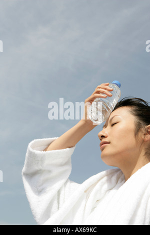 Eine Frau im Bademantel, eine Flasche Wasser auf der Stirn zu platzieren Stockfoto