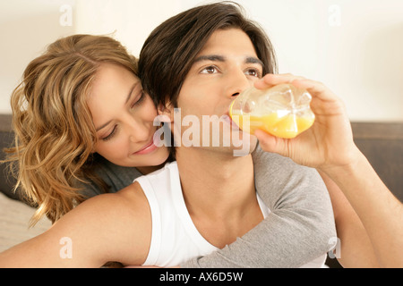 Junger Mann, Trinkwasser in Flaschen Saft, Frau umarmte ihn von hinten Stockfoto