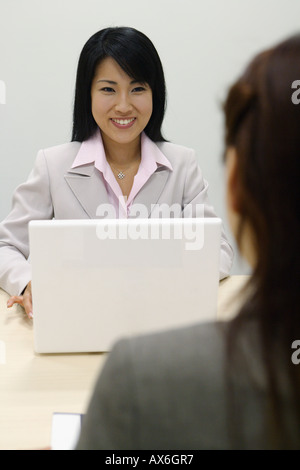 Eine Frau, die Arbeit an ihrem Laptop lächelt ihr Kollege Stockfoto