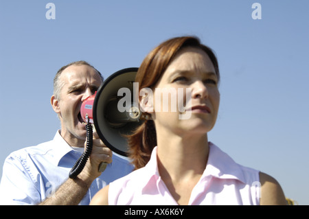 Frau mit Mann schreien in Megaphon hinter ihr in Nahaufnahme Stockfoto