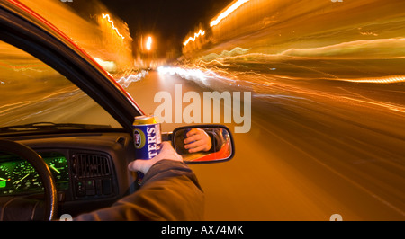 Trinken Sie, fahren Sie nachts, während Sie eine Dose Bier in der Hand halten, und zeigen Sie bei Zeitlupenaufnahmen verwackelte Lichter Stockfoto