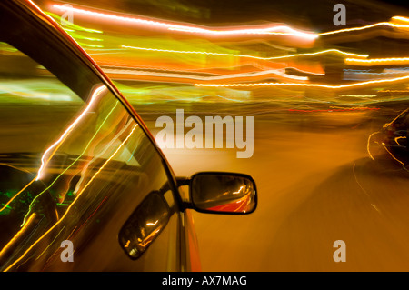 Nachts fahren, während Sie eine Dose Bier halten und bei Zeitlupenaufnahmen verschwommene Streifen von Straßenlaternen und Ladenbeleuchtung zeigen Stockfoto