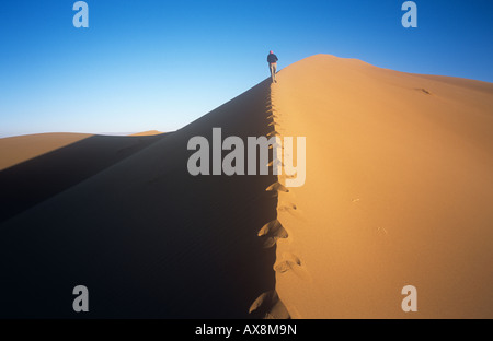 Frau zu Fuß auf dem Kamm einer Düne kurz nach Sonnenaufgang, Erg Chigaga, Sahara, Marokko. Stockfoto