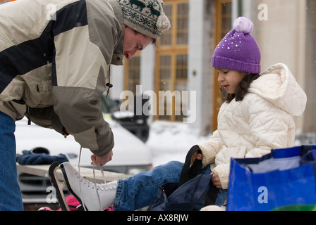 Ein junges Mädchen schaut zu, wie ihr Vater hilft auf Schlittschuhe während Kingston jährliche FebFest Winteraktivitäten binden Stockfoto