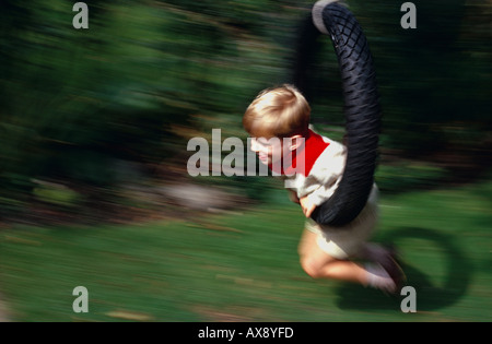 Vier Jahre alter Junge mit Hilfe eines Reifens hängen von einem Baum als eine Schaukel. Vor allem grünen Hintergrund unscharf. Stockfoto