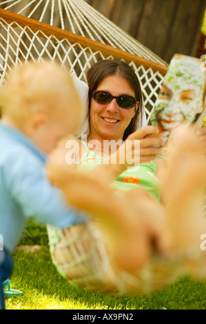 Frau zum Entspannen in der Hängematte im Garten, liest eine Zeitschrift, kleine Junge stand Nect, Hängematte, Entspannung Stockfoto