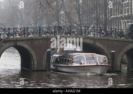 Eine Kanalboot geht unter einer Brücke in Amsterdam Stockfoto