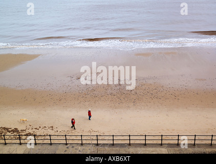 Ein paar am Strand von Mundesley bei Ebbe mit ihrem Hund spazieren Stockfoto