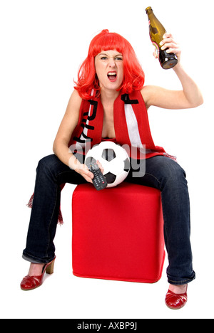 weibliche Fußball-Fan mit einer roten Perücke, eine Flasche Bier und Fernbedienung ein Fußballspiel ansehen Stockfoto