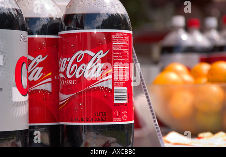 Nahaufnahme einer Coca-Cola-Flasche mit einer Schüssel frischer Früchte im Hintergrund, USA symbolisieren den Kontrast zwischen verarbeiteten Erfrischungen und natürlicher Ernährung. Stockfoto