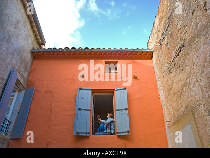 Junger Mann, sitzend von einem alten Fenster mit Glas Wein, Languedoc-Roussillon, Frankreich Stockfoto