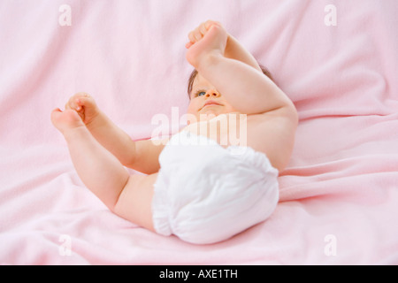 Babymädchen (6-9 Monate) auf Bett, Zehen berühren Stockfoto