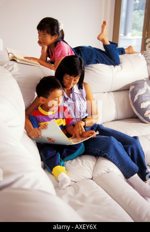 Eine japanische amerikanische Mutter lehrt ihren 4 Jahre alten Sohn zu lesen, während ihre 7-jährige Tochter ihr eigenes Buch liest Stockfoto