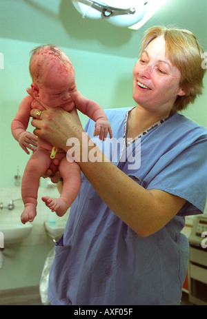 Hebamme hochhalten Neugeborenes geprüft und abgewogen werden. Stockfoto