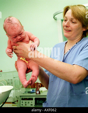 Hebamme hochhalten Neugeborenes geprüft und abgewogen werden. Stockfoto