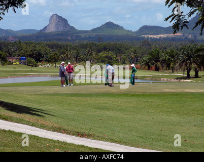 3 westliche Männer auf dem Grün mit 2 weibliche Transportgestelle Pheonix Golf und Country Club Pattaya Thailand mit Berg Buddha graviert Hügel im Hintergrund Stockfoto